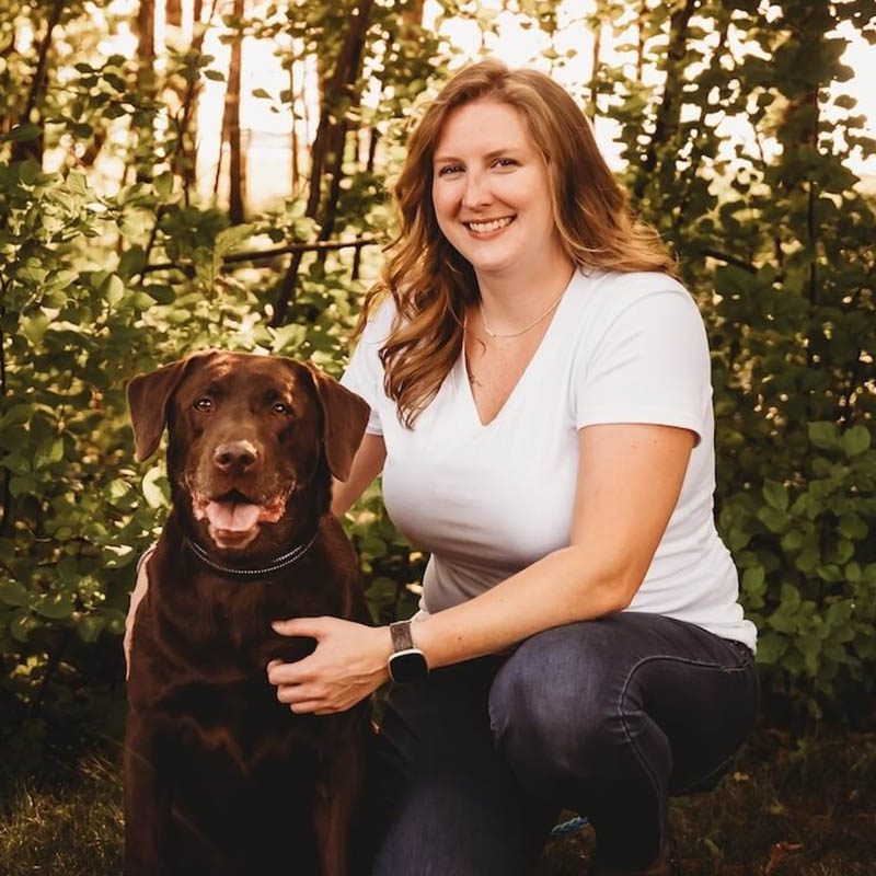 Amanda with her brown dog in the woods