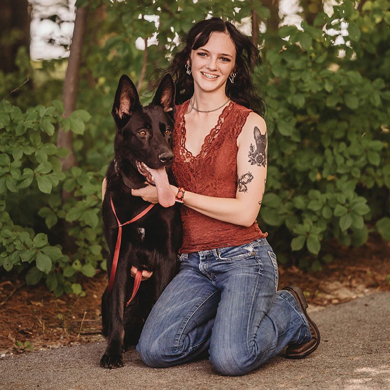 Hannah kneeling by her dog in the woods