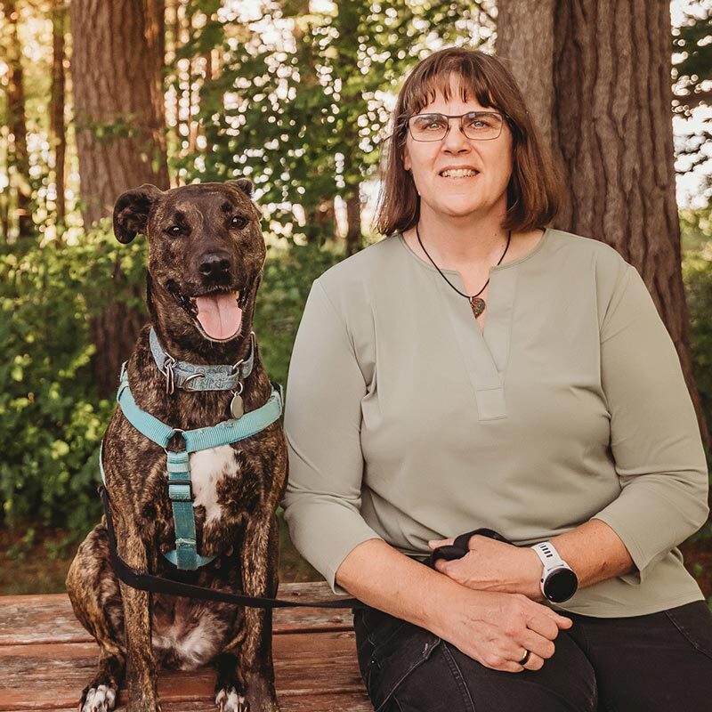 Dr Diana Raddatz sitting in the woods with her dog